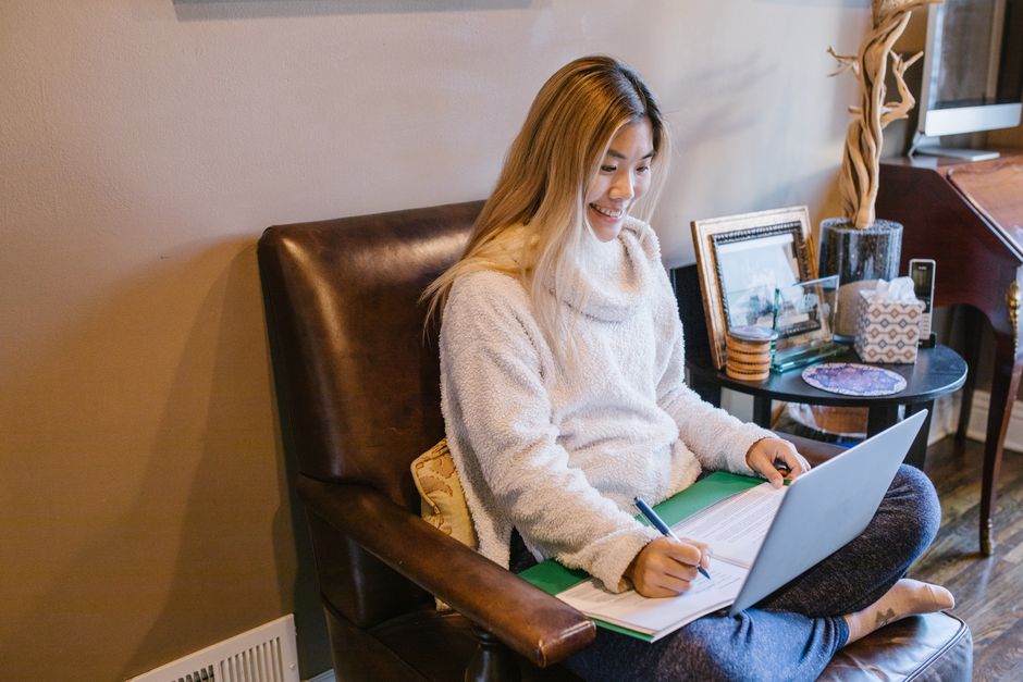Personne étudiant en ligne à la maison, prenant des notes devant un ordinateur portable