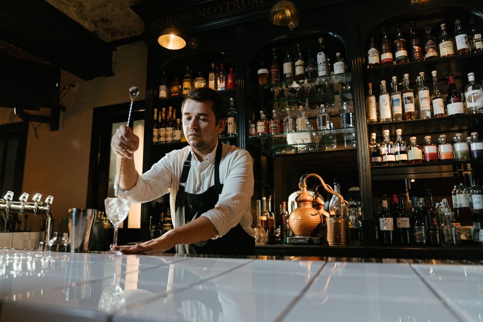 Barman préparant un cocktail derrière un comptoir bien garni